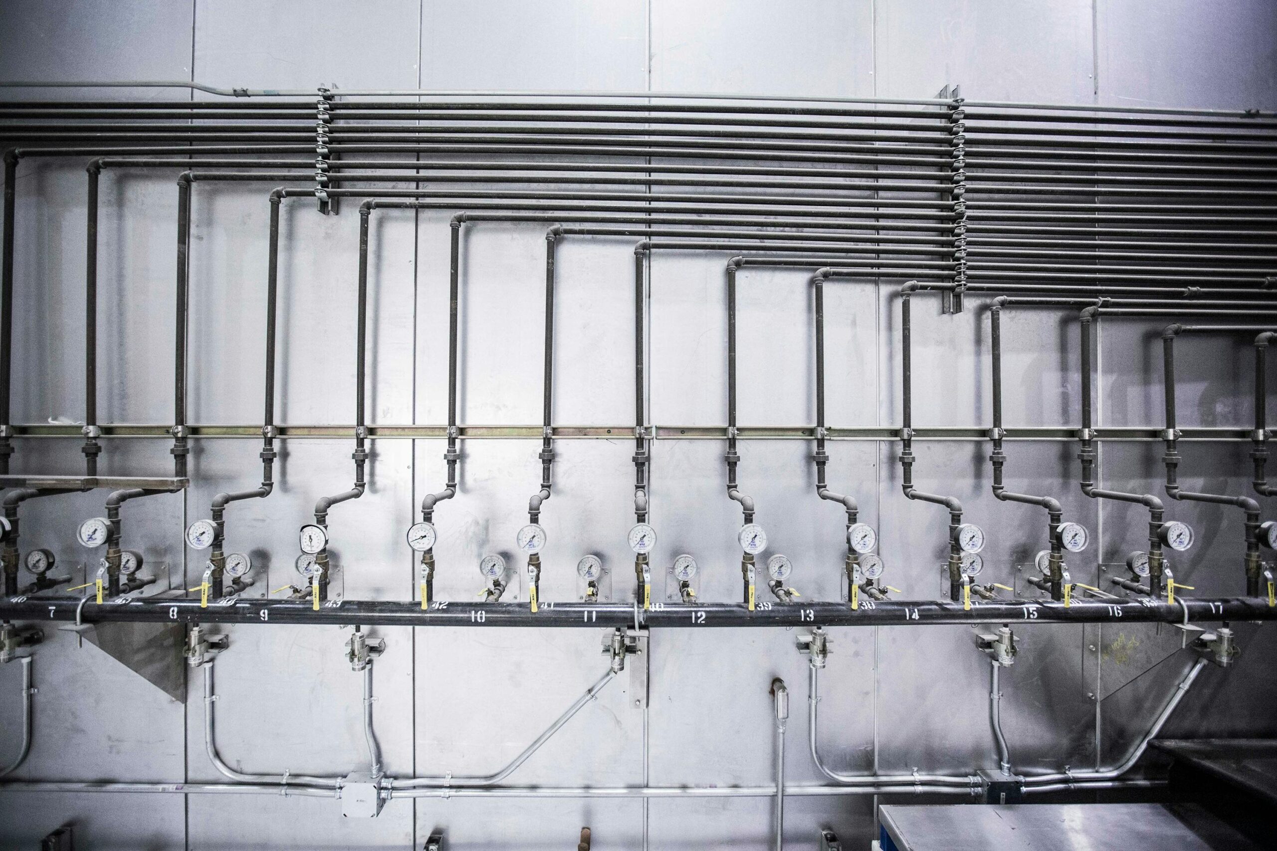 Rows of metal pipes and shutoff valves mounted on a wall