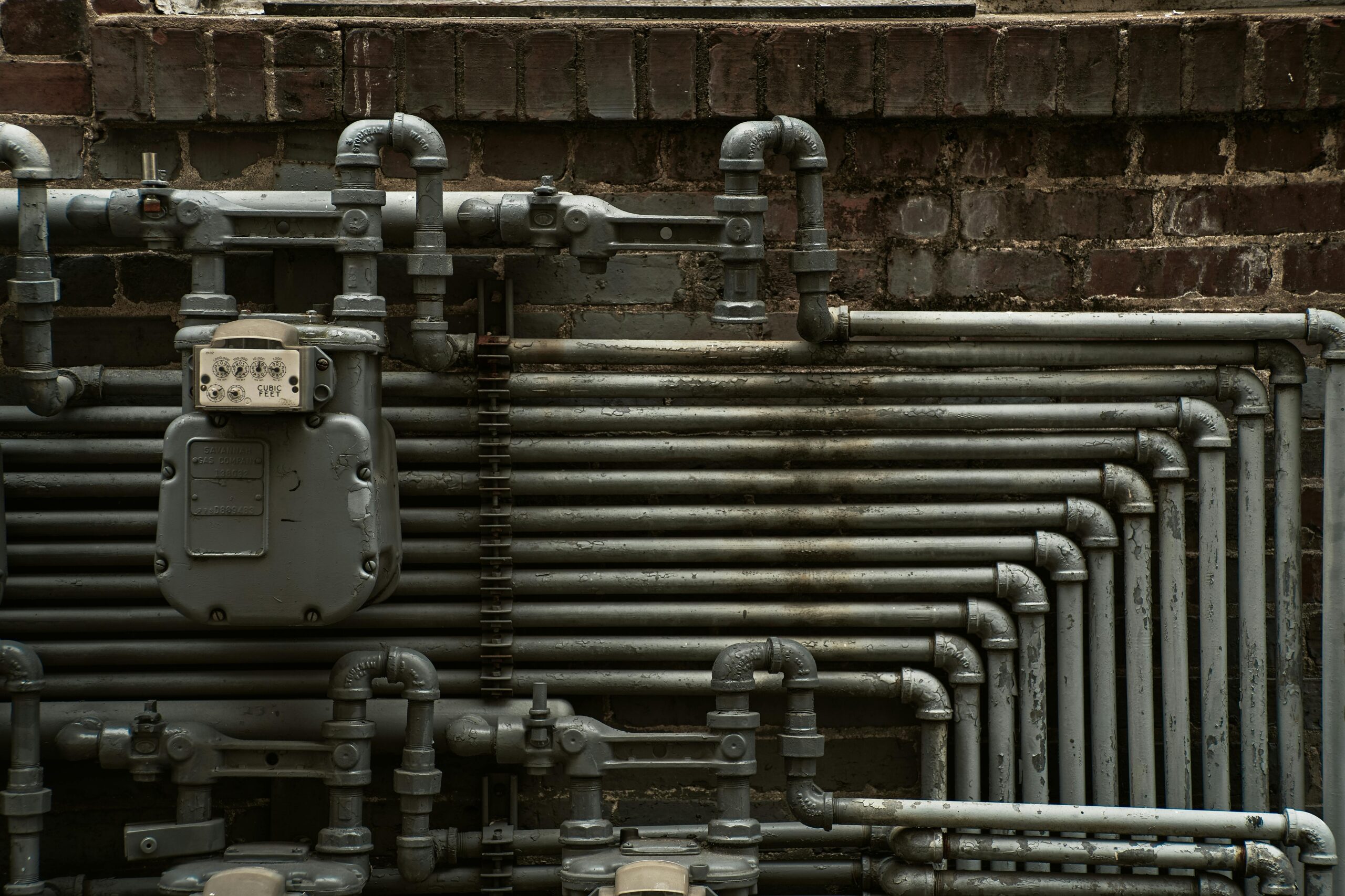 Gas meter and steel gas lines running along a brick wall