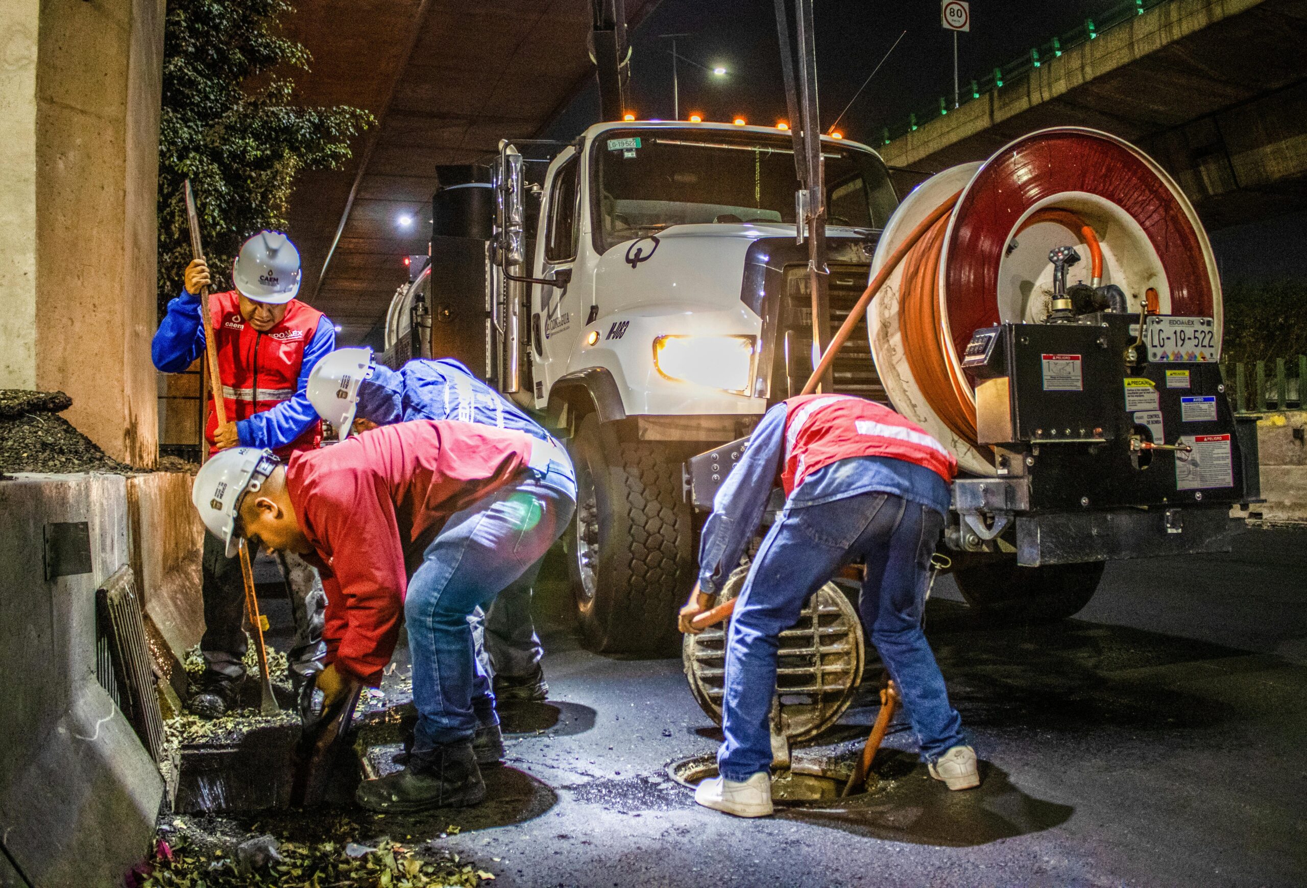 Crew using a sewer jetting truck to clear a sewer line at night