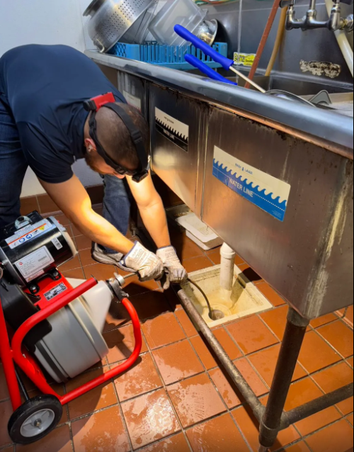 Plumber using a drain cleaning machine on a commercial kitchen sink drain