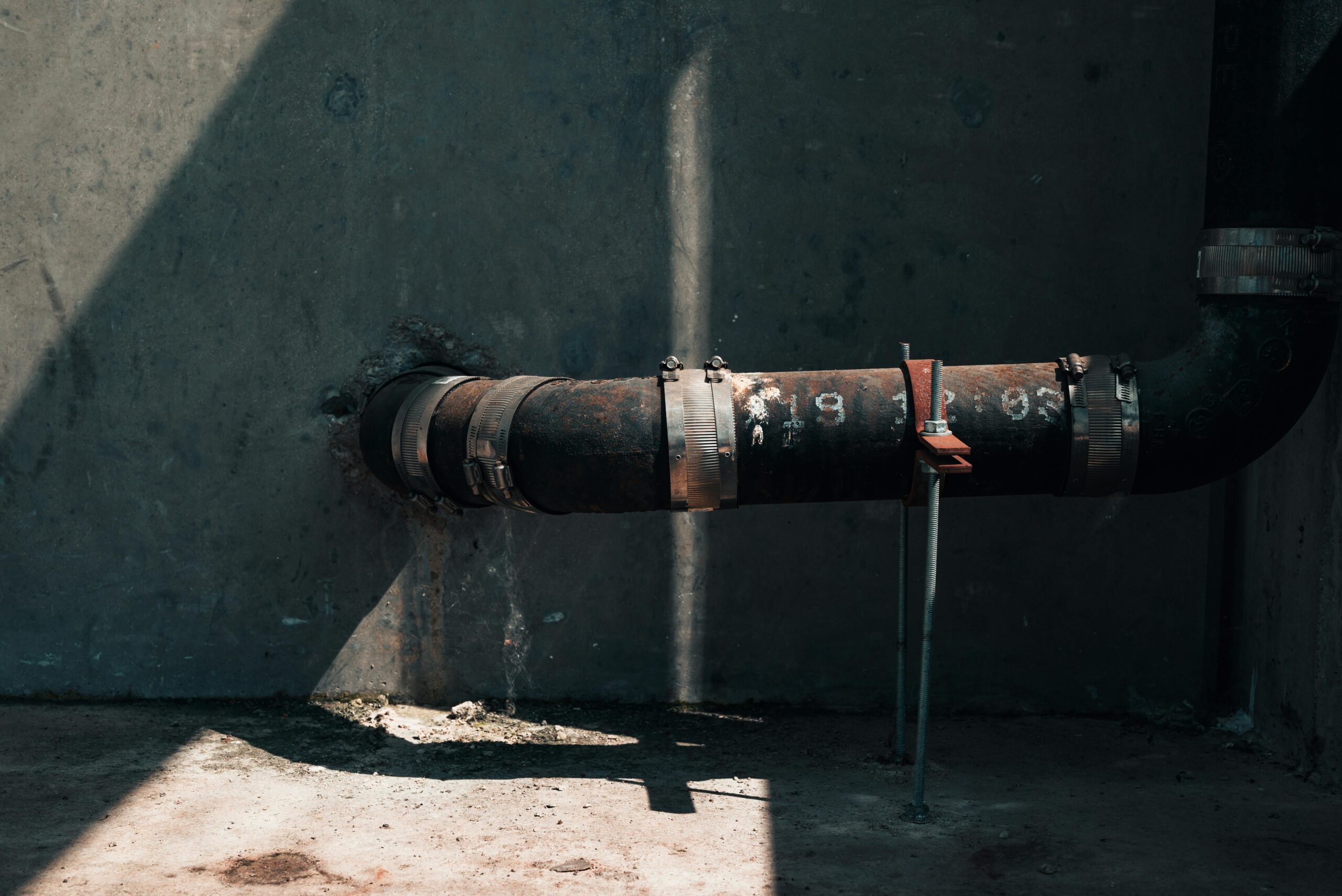 Leaking pipe dripping water along a concrete wall